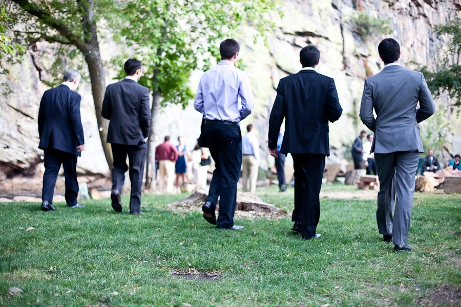 a line of five men in suits walk away from the camera