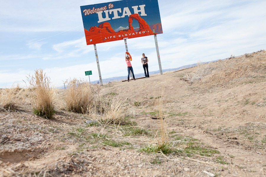 two women pose under a sign that says welcome to utah