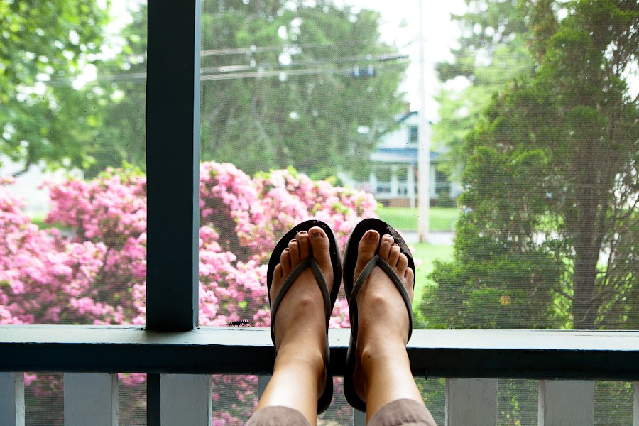 flip flop feet sit on a ledge in front of pink bushes