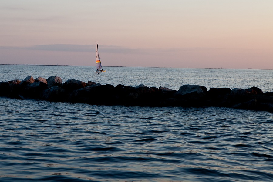 a sailboat sails on calm water under a pink sky