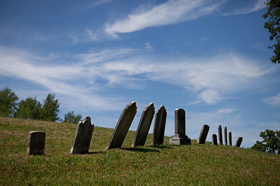 a row of rickety old tombstones with grass and blue skies