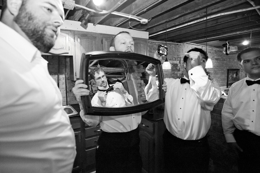 black and white of a groom looking in a mirror while adjusting his bowtie