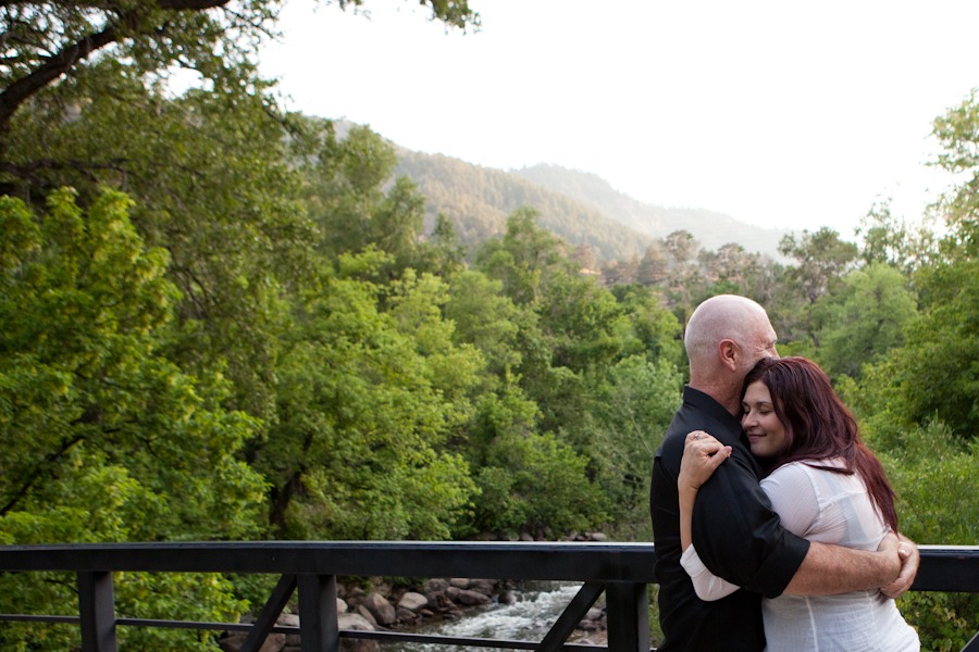 a woman with red hair and a man hug on a bridge in front of mountains