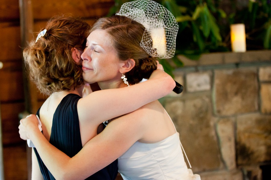 a bride hugs her sister who holds a microphone