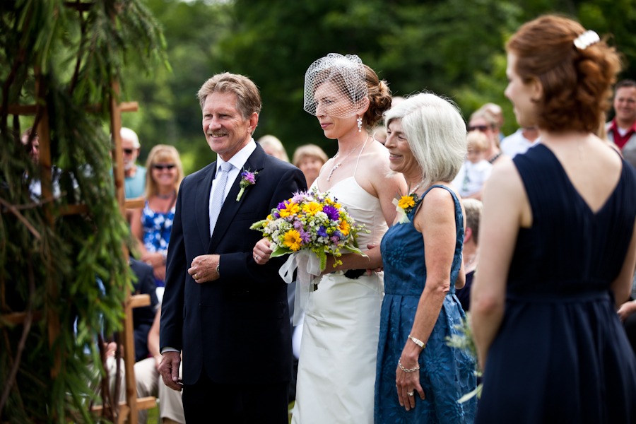 parents walk their daughter down the aisle at her outdoor wedding ceremony