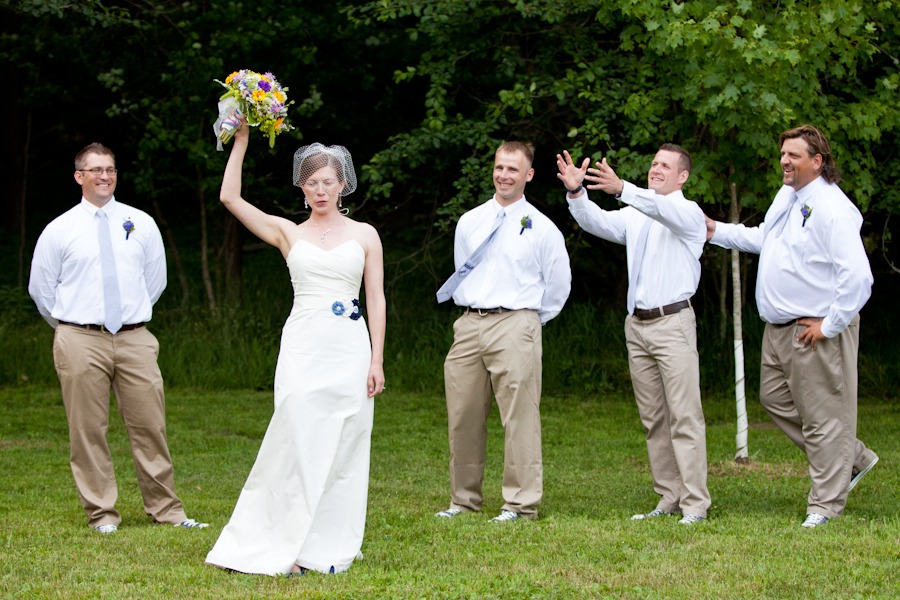 a bride holds her bouquet up in the air in front of a line of groomsmen