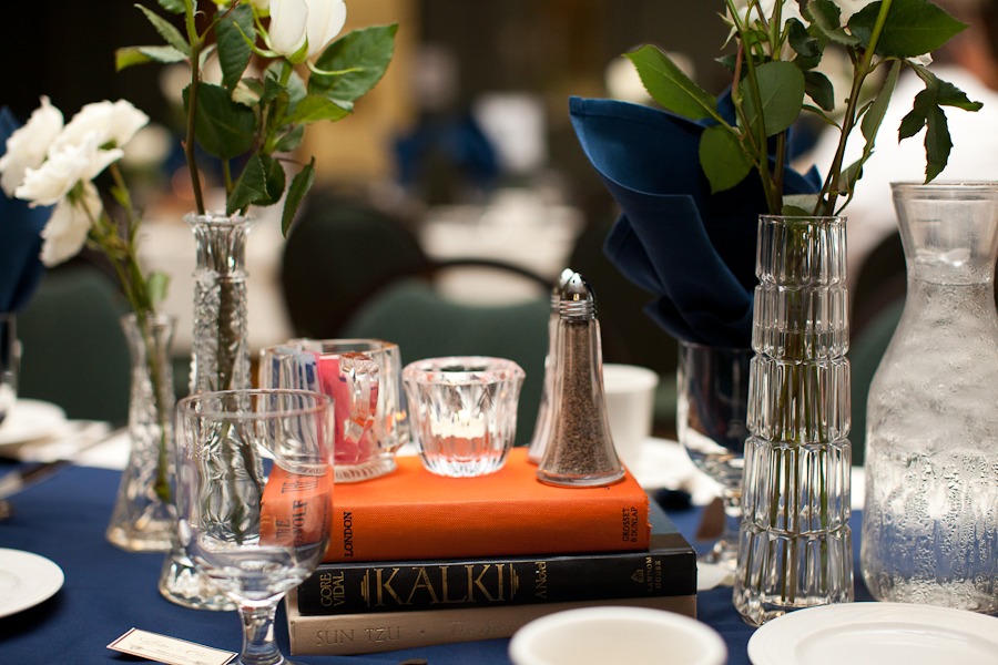 a tablescape at a wedding reception featuring old books and crystal vases with white roses