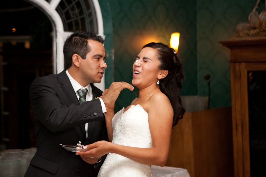 a groom puts icing on his bride's nose after cutting the wedding cake in a green room