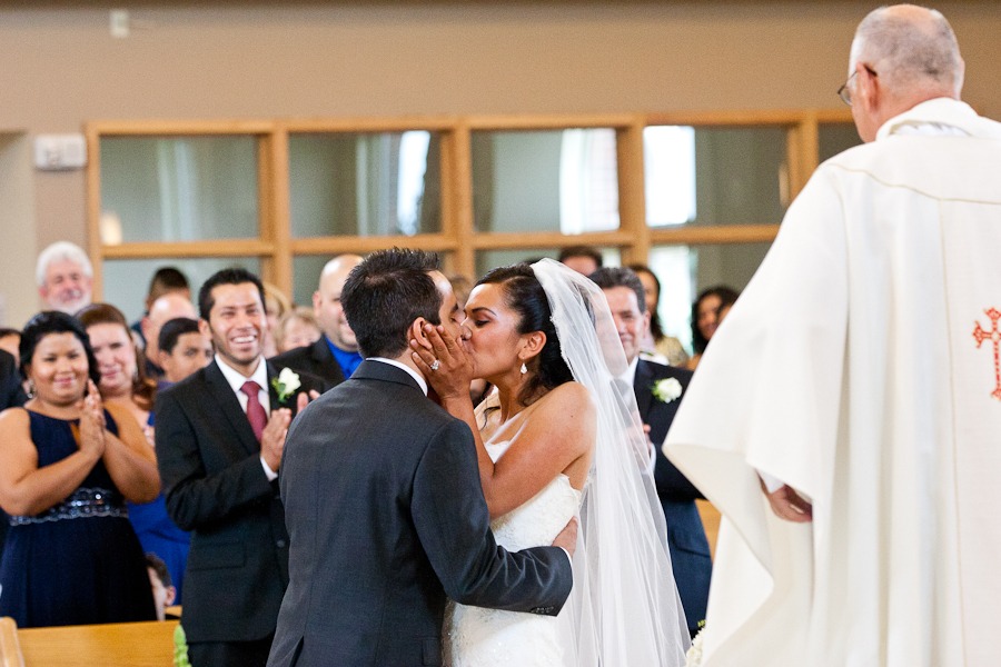 a wedding couple kiss at an altar while guests clap