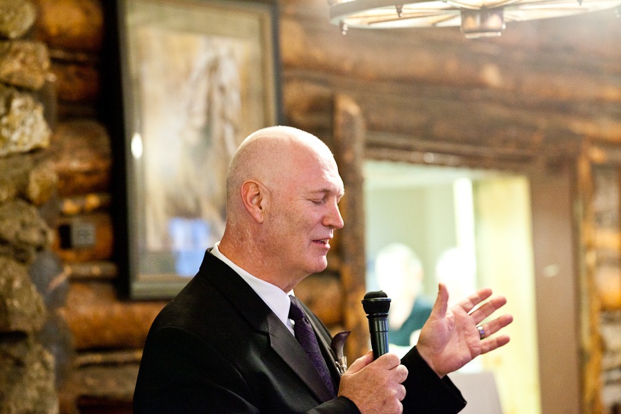 a groom closes his eyes as he speaks into a mic in a log room