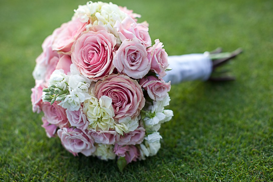 a wedding bouquet of pink and white flowers sits on a green lawn