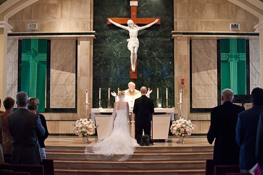 a bride and groom kneel at an altar