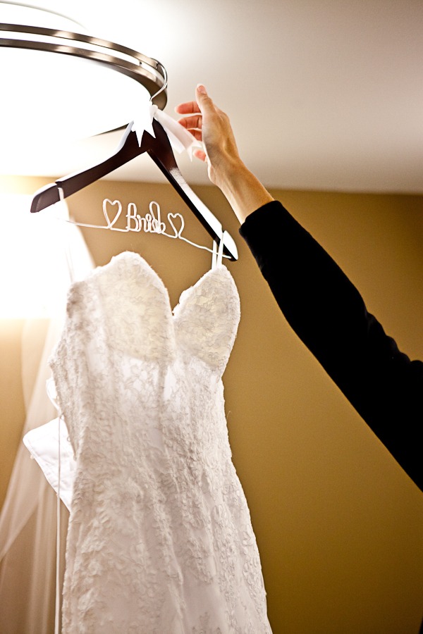 a hand reaches for a wedding dress that hangs from a hanger that says BRIDE