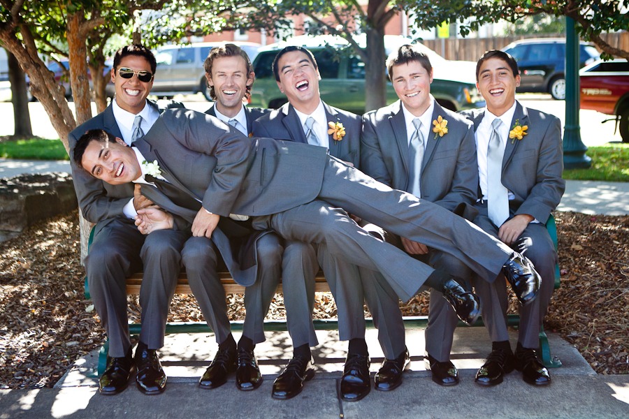 five groomsmen sitting on a bench hold a groom and laugh