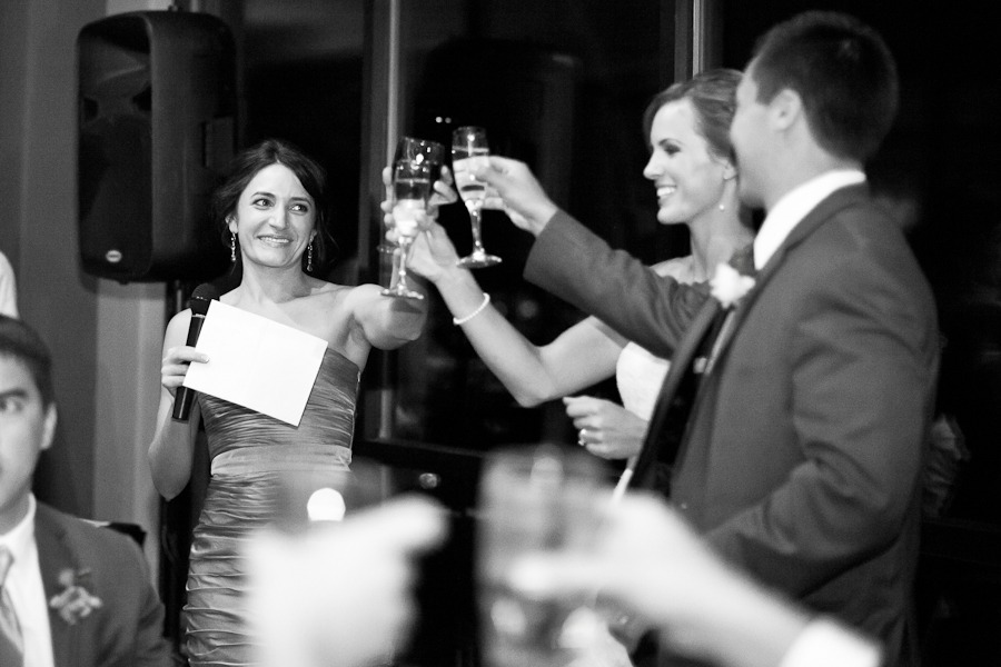 black and white image of a bridesmaid raising her champagne glass to clink the bride and groom