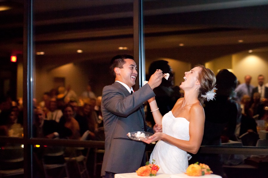 bride and groom laugh as they feed each other cake