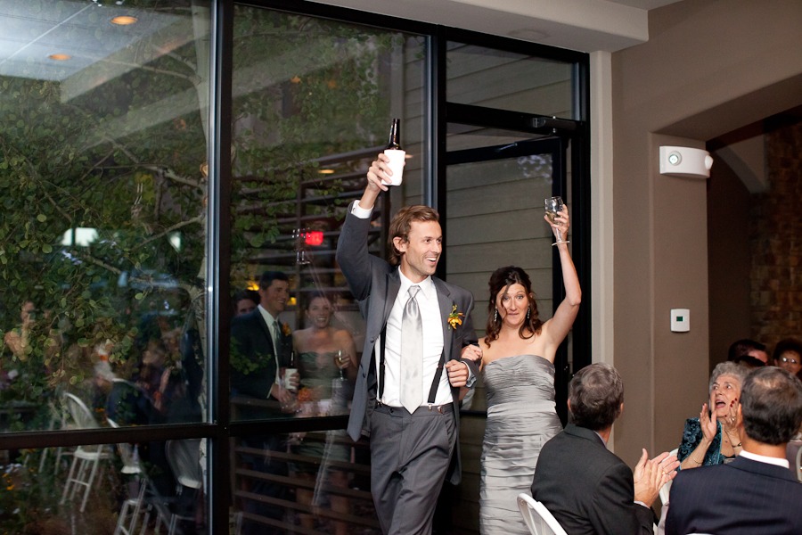 a man in a suit with suspenders and a woman in a gray dress enter a room with arms raised