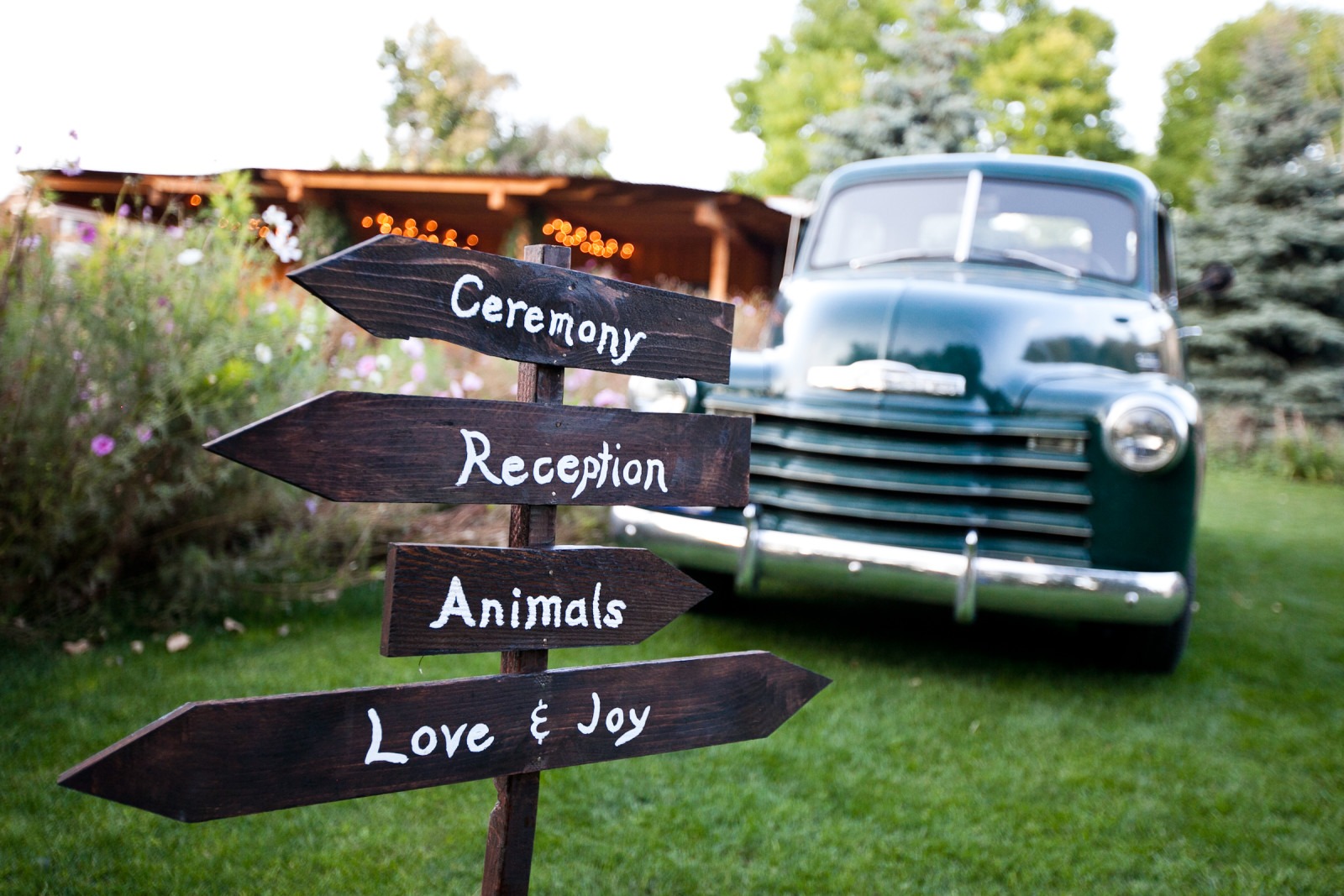 wooden sign with white words painted on it that say reception, animals, love&joy, ceremony in front of an old pick up truck
