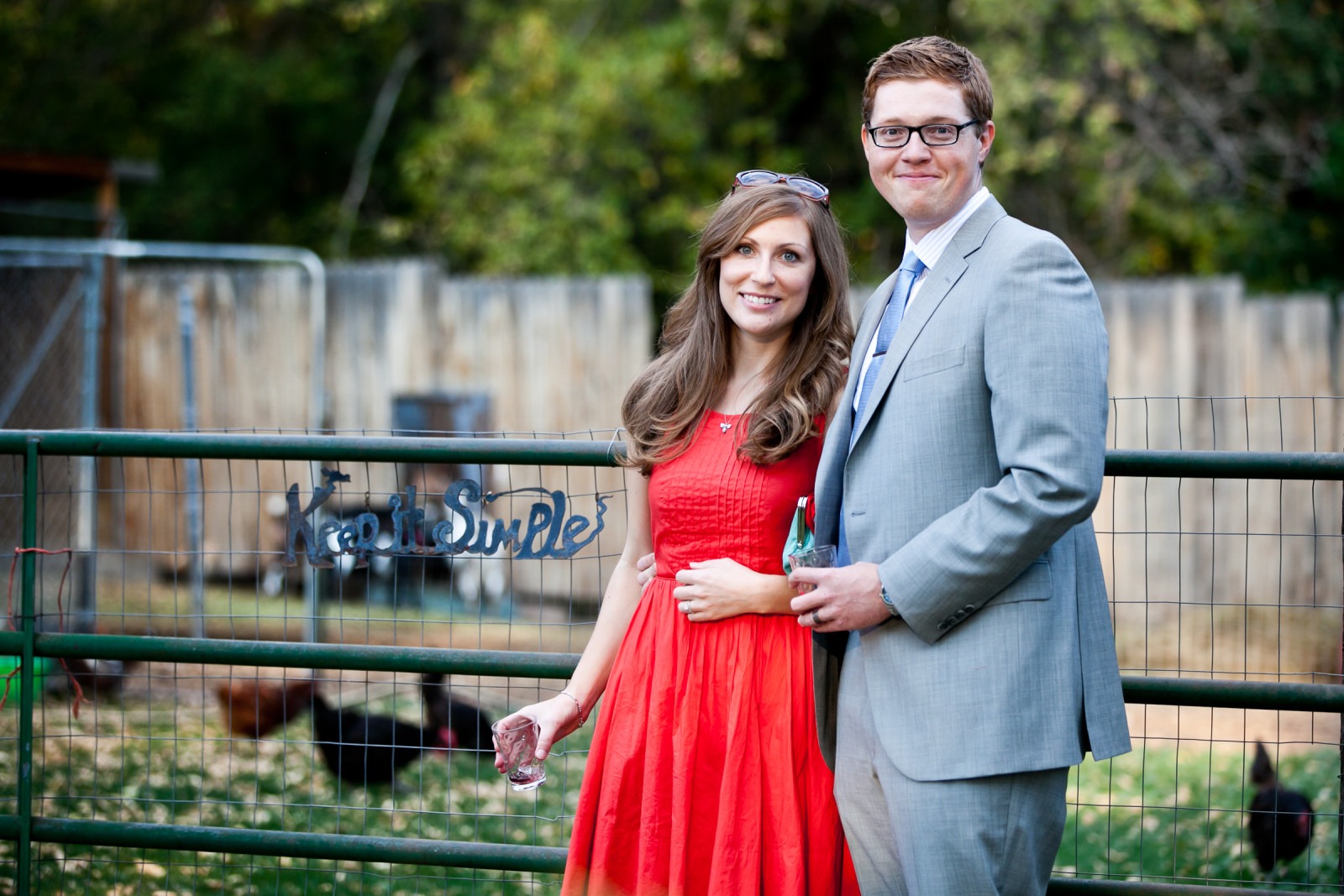 a man in a suit and a woman in a red dress stand in front of a fence