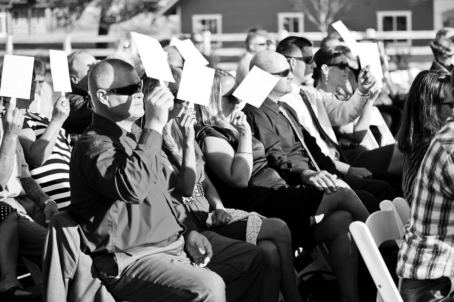 seated wedding guests hold up fans to block the sun
