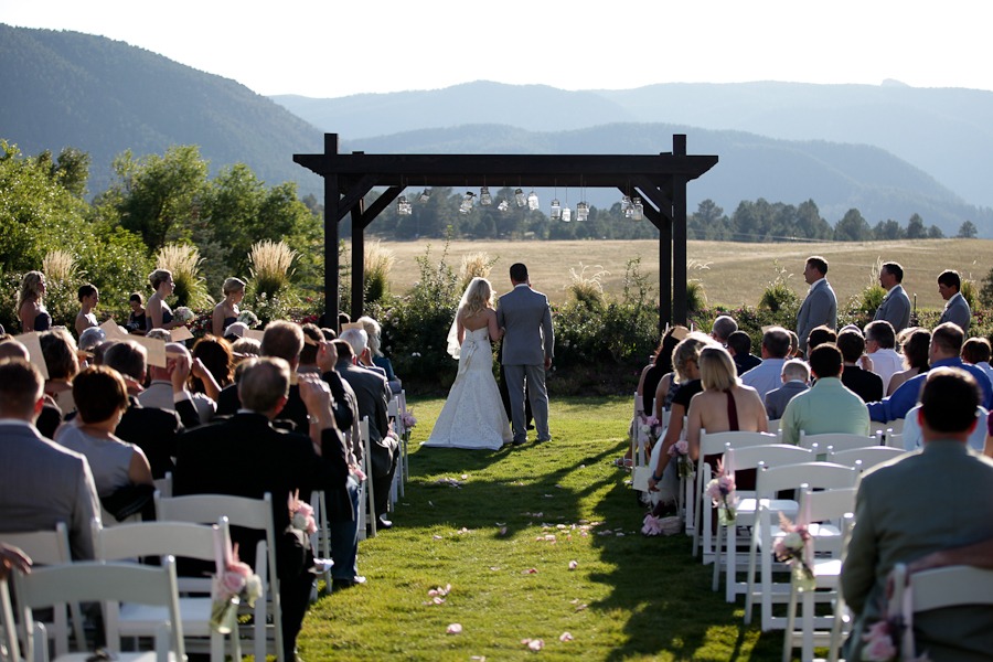 a bride and groom stand at the front of a grassy green aisle with mountain views