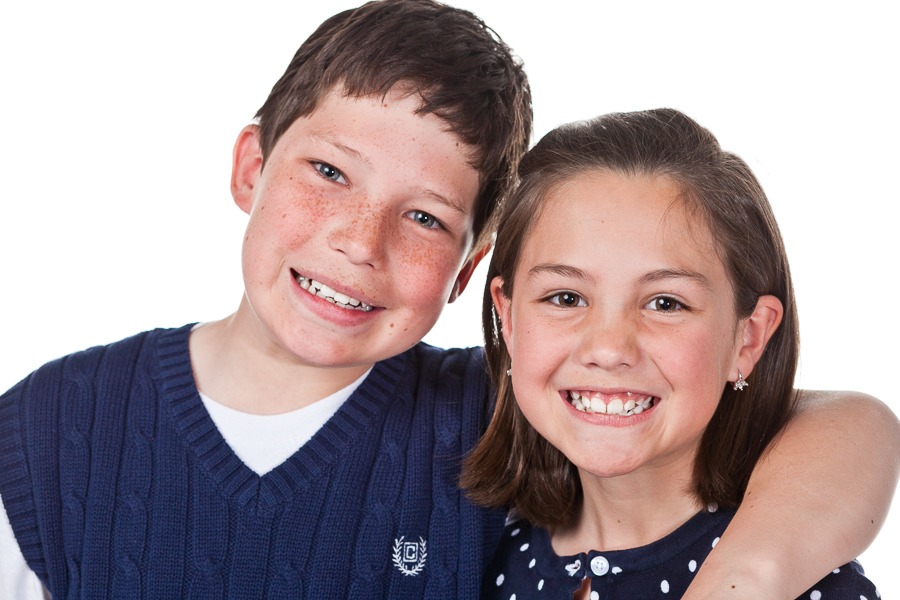 siblings smile for the camera against a bright white ground