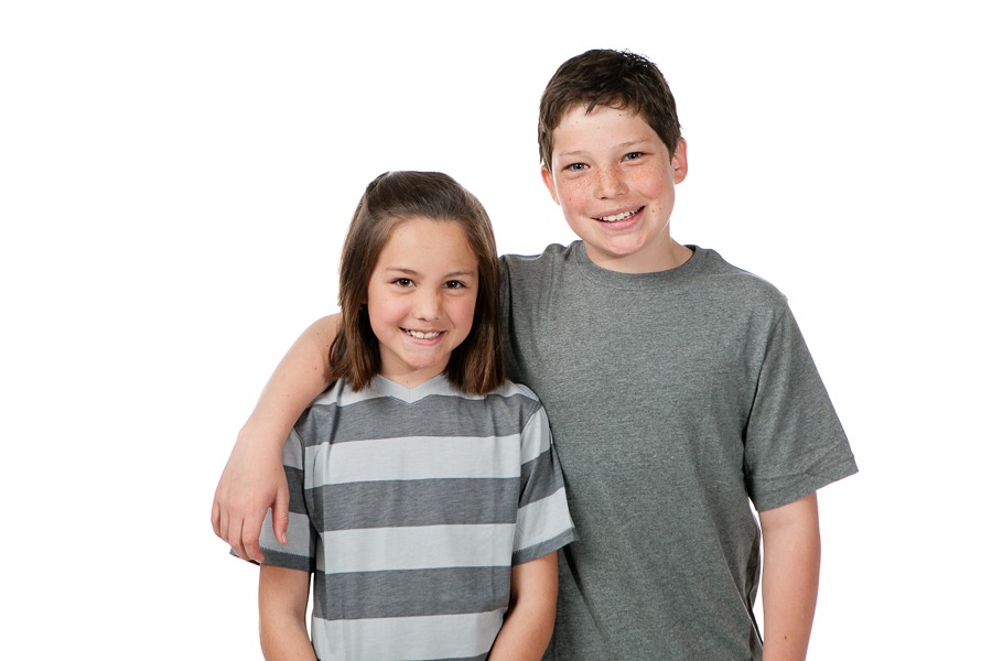 a big brother wraps an arm around his little sister in a photography studio