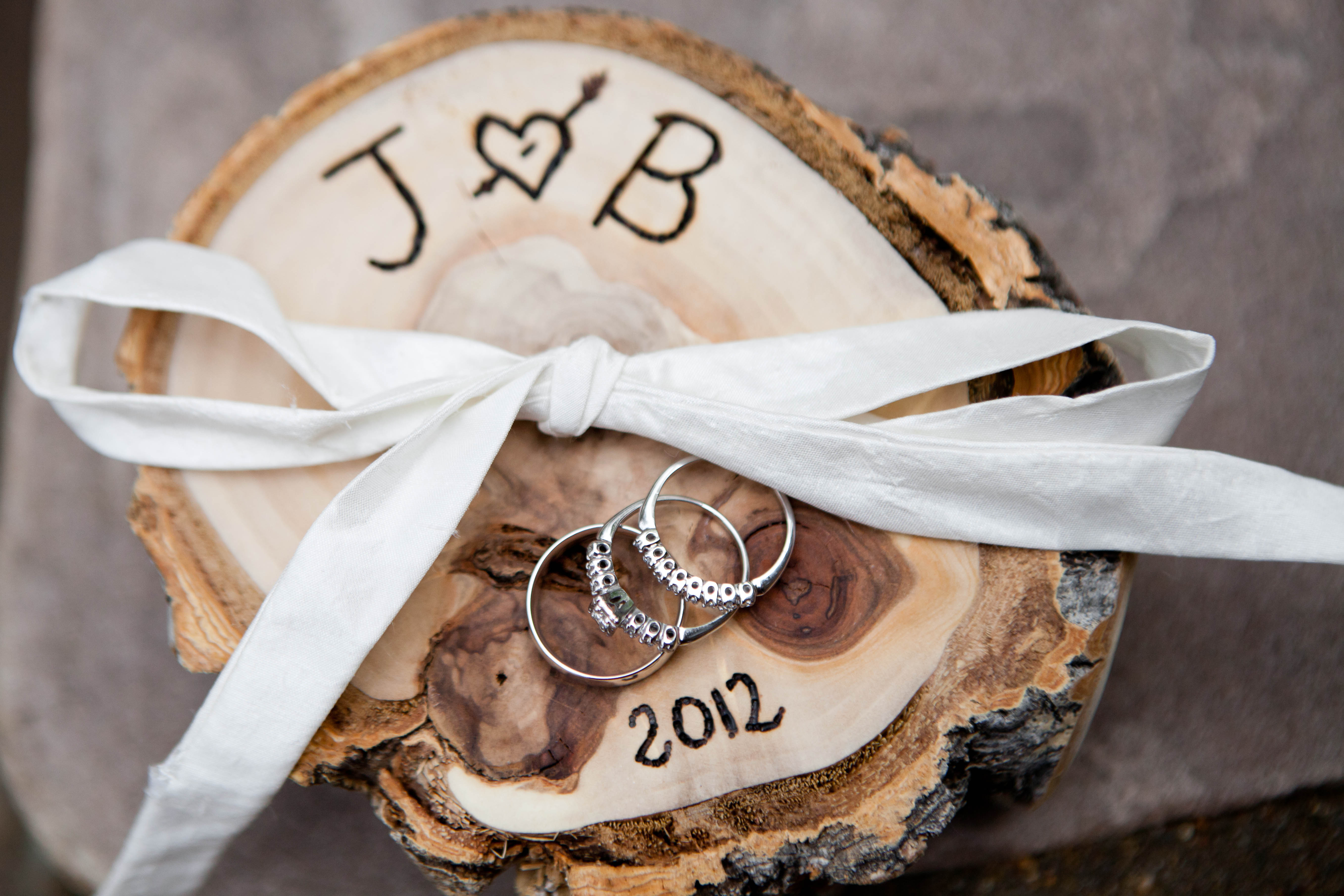three rings sit on a piece of wood that is engraved with the initials J and B and the year 2012