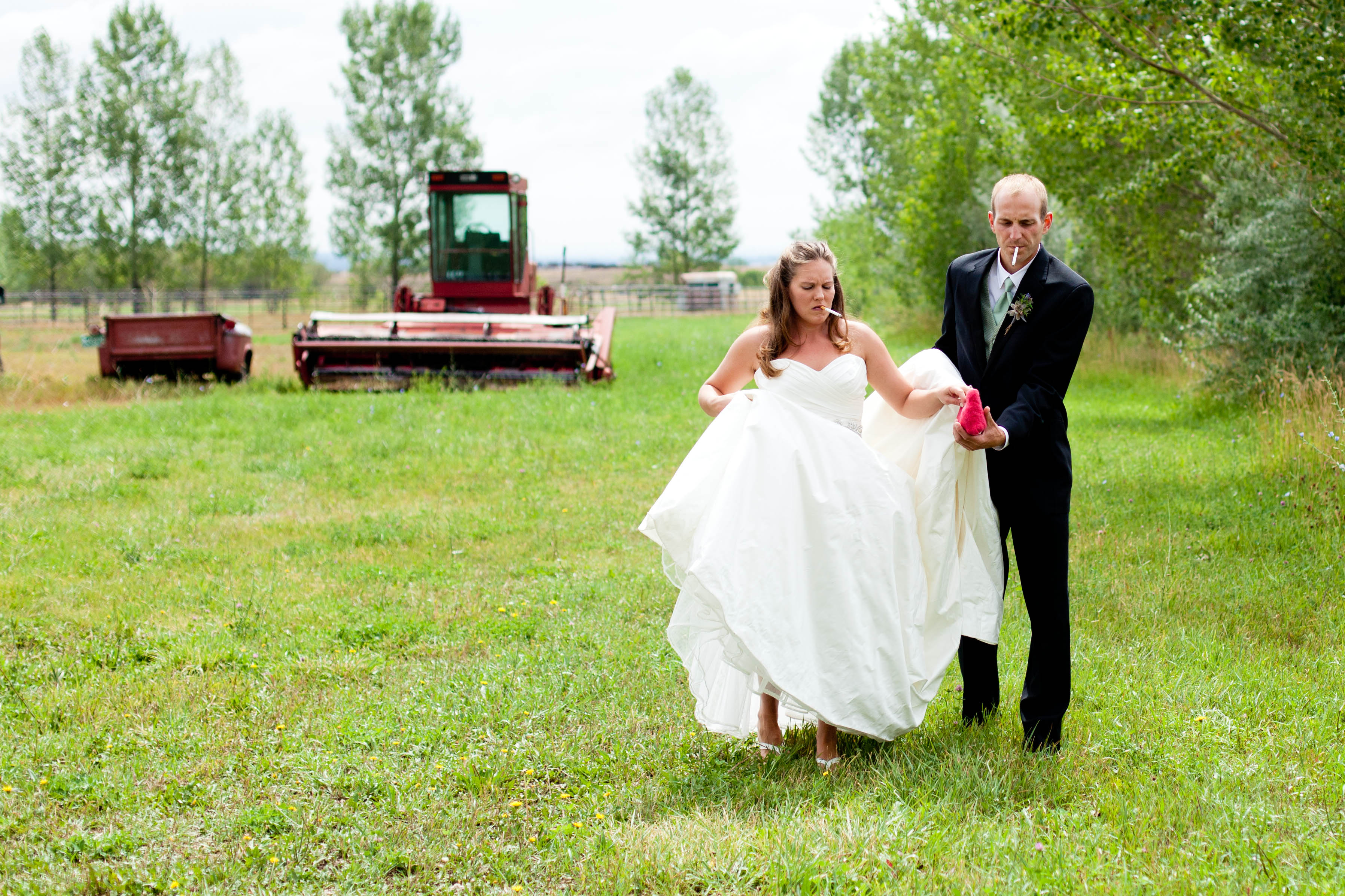 a bride and groom smoke while walking away from red farm equipment