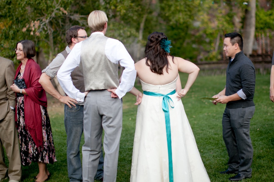a bride and groom stand away from the camera with their hands on their hips