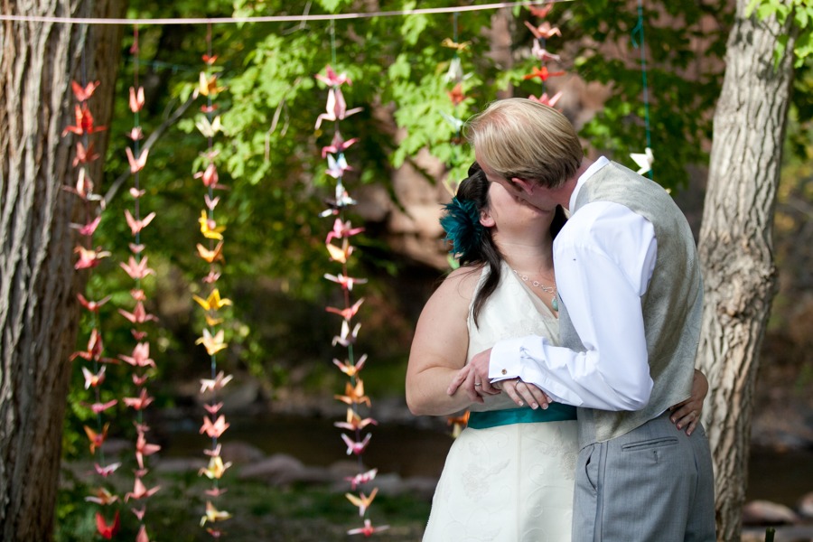 bride and groom kiss in front of paper cranes