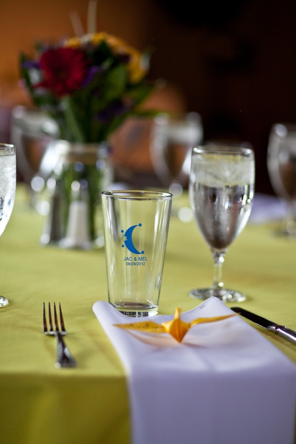 a pint glass and yellow crane sit at a wedding reception table