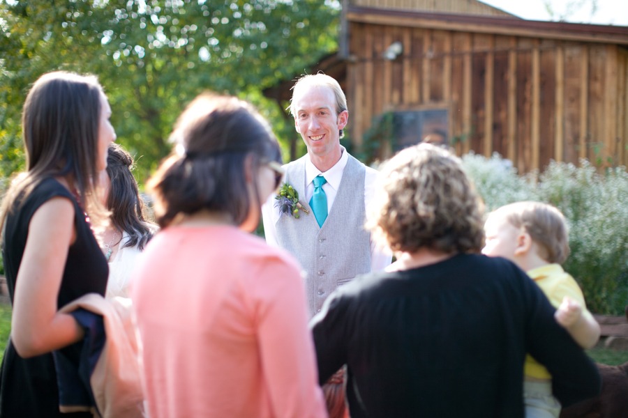 a groom in a gray vest chats with wedding guests