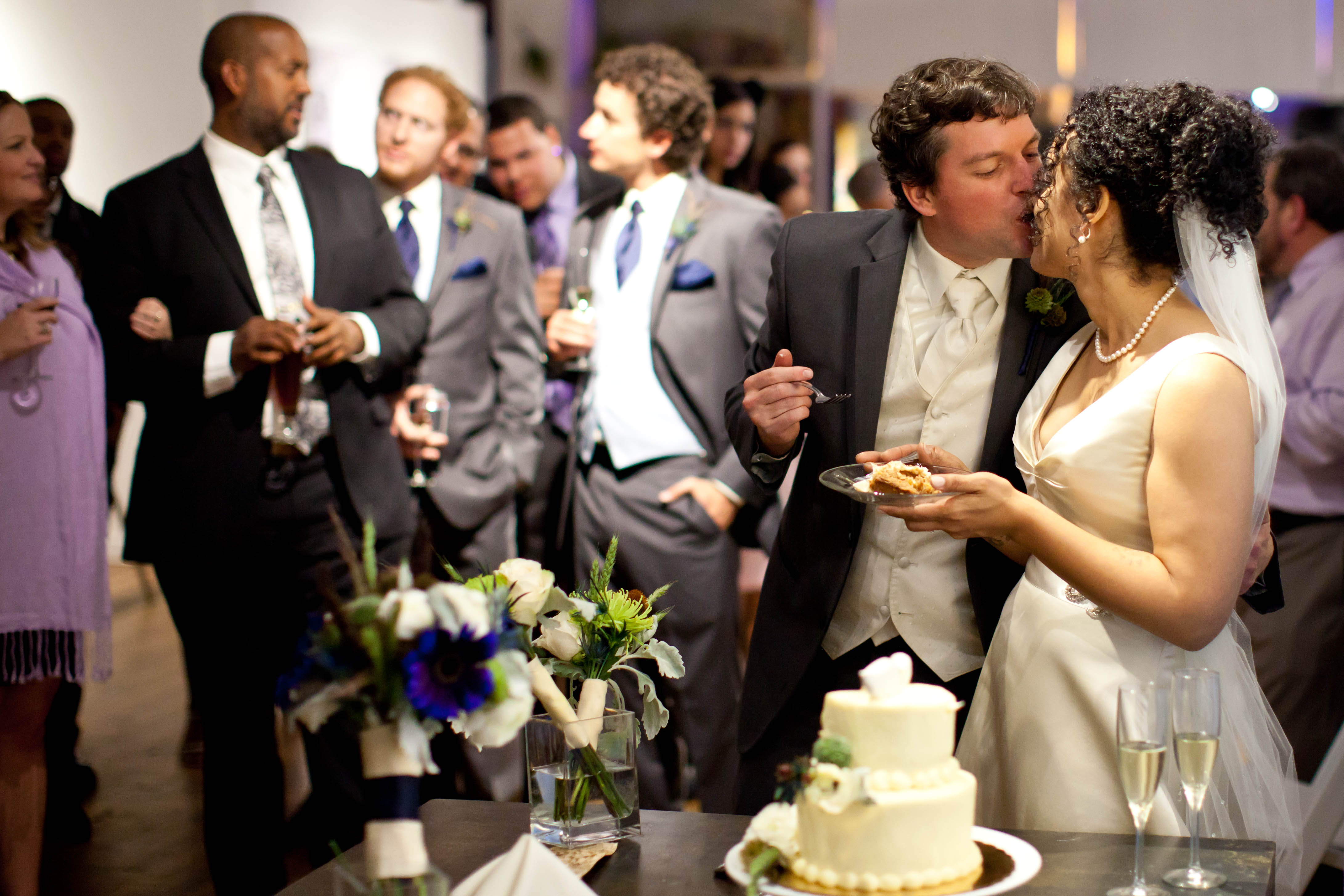a bride and groom kiss while holding a piece of cake