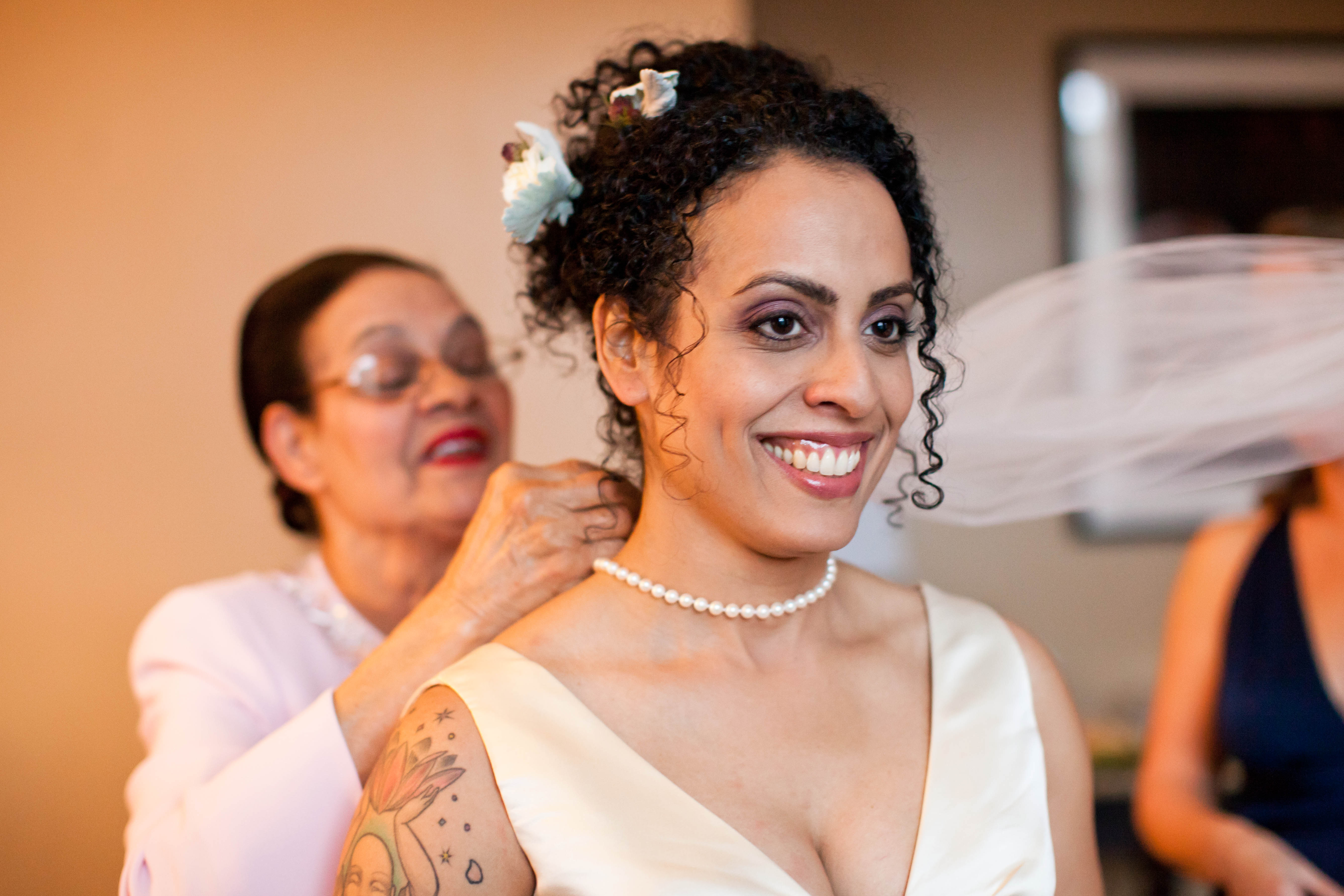 a woman puts a pearl necklace on a bride