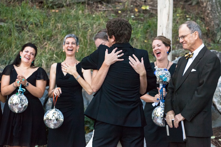 a wedding couple hug while bridesmaids holding disco balls laugh