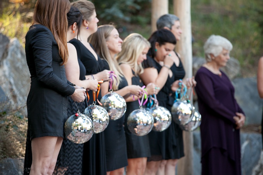 a row of bridesmaids wearing black dresses and holding disco balls