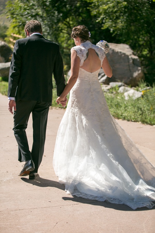 a bride with a beauitful wedding dress holds hands with a groom as they walk away from camera