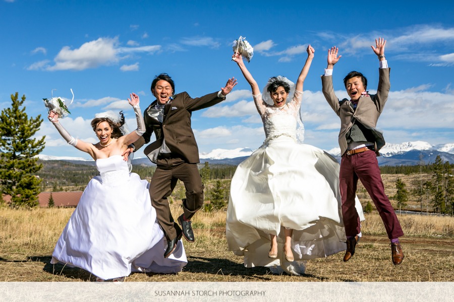 two brides and two grooms jump up in the air under blue skies