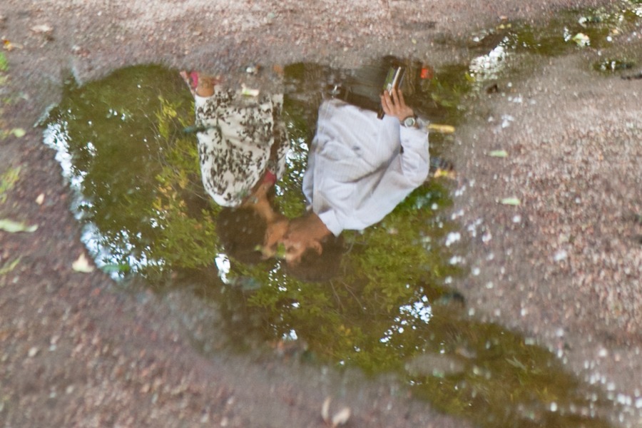 the reflection of a couple kissing appears in a puddle of water