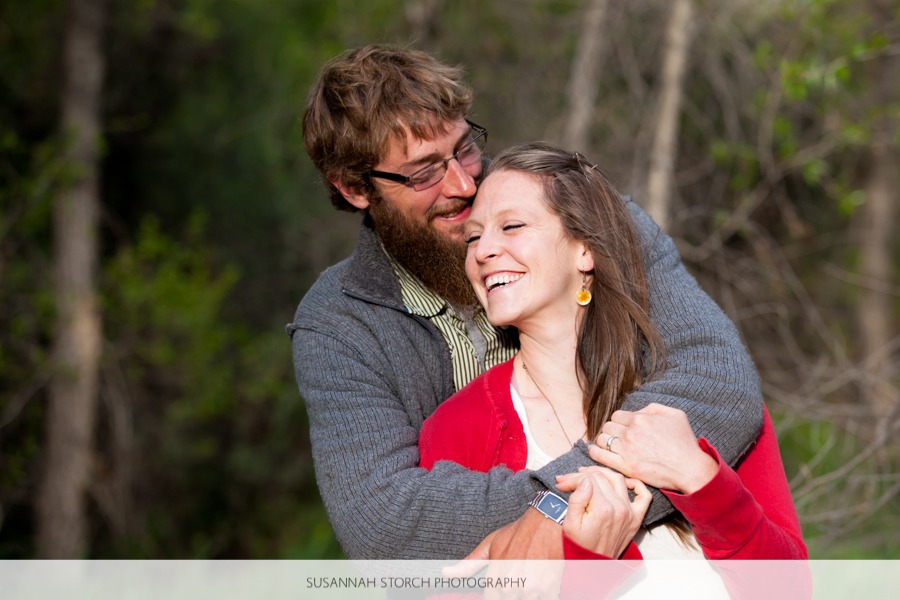 a man with a beard and eyeglasses gives a woman in a red sweater a big bear hug
