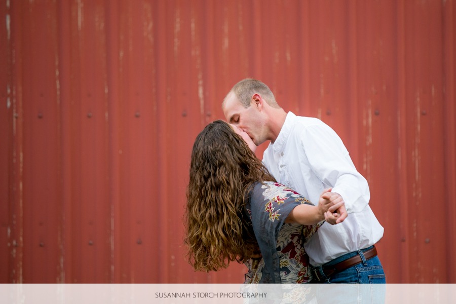 a man and woman kiss in front of a rad barn