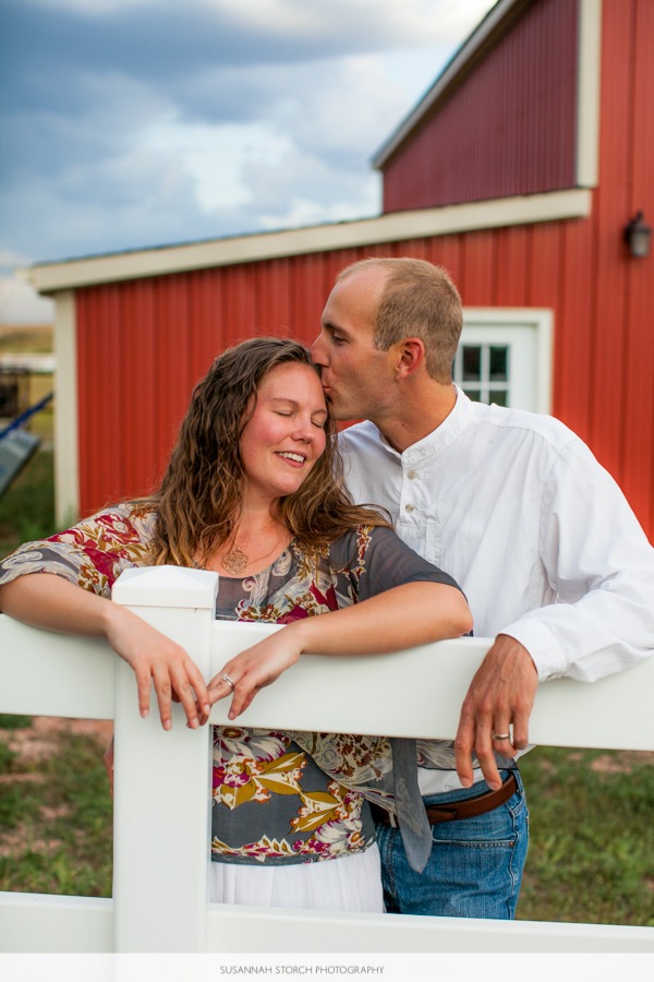 man kisses a woman in front of a red barn