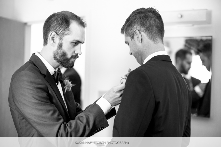 black and white photo of a groom putting a boutinierre on a man