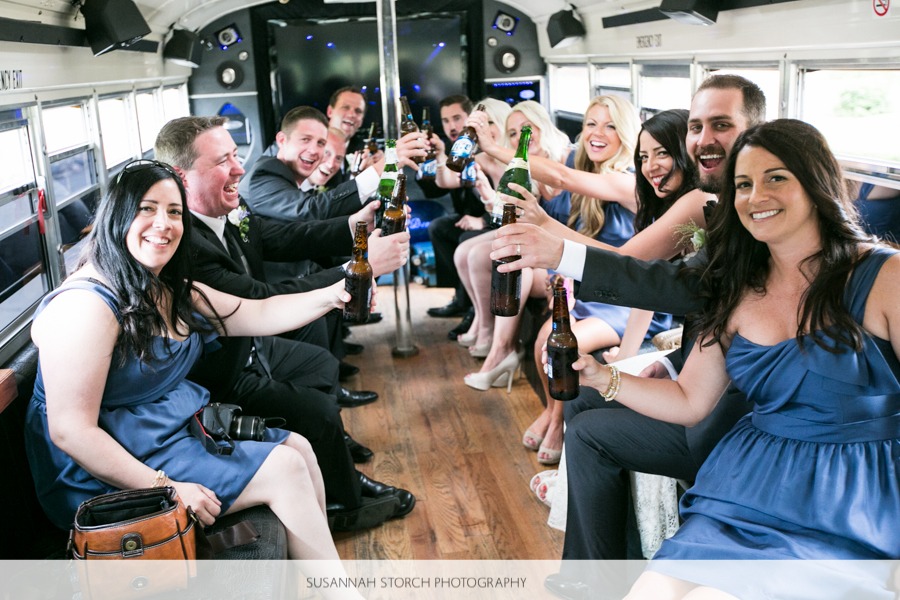 women in blue and men in suits cheers with bottles of beer while on a bus