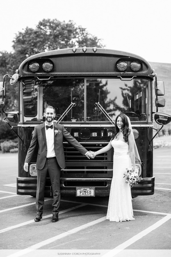 black and white of a bride and groom holding hands in front of a Bluebird bus in a parking lot
