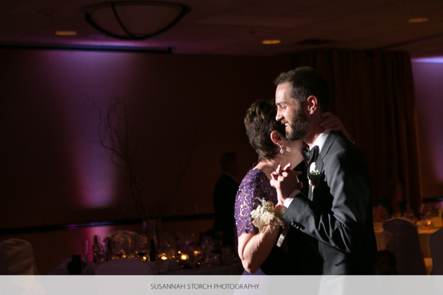 a groom dances with his mother in front of purple uplighting