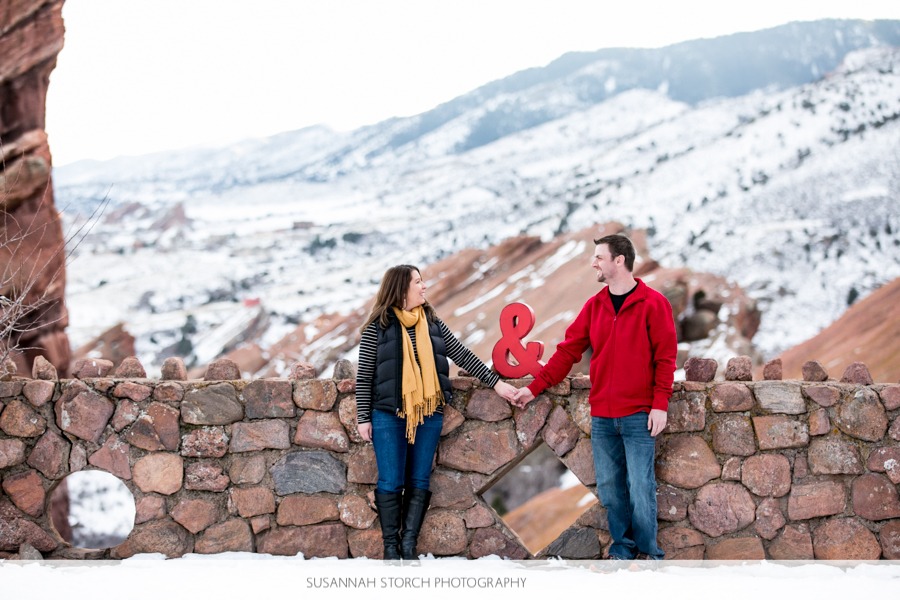 a couple hold hands in front of rock wall and snowy mountain