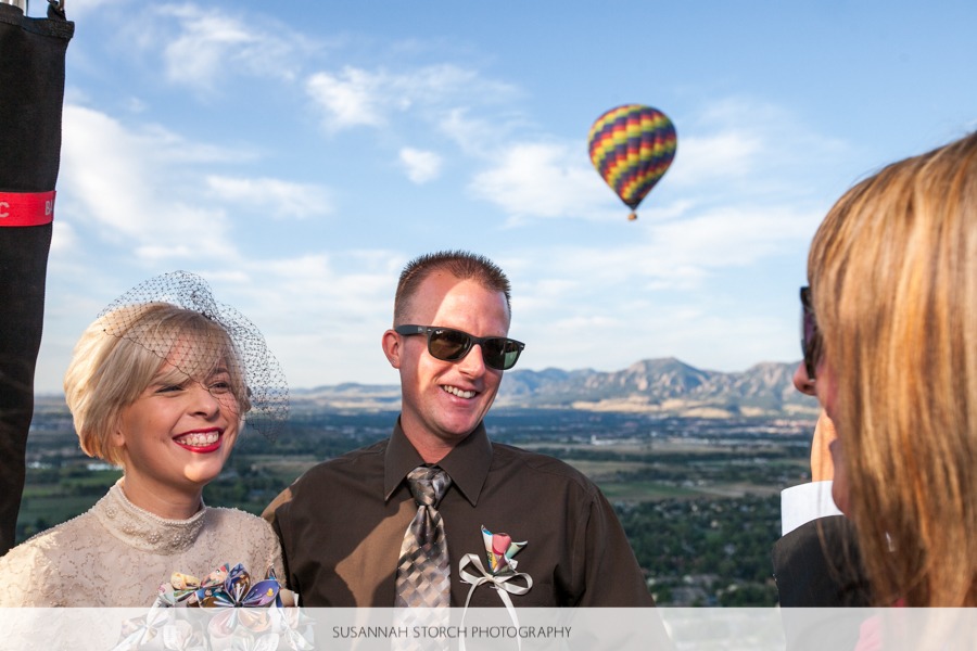 a bride and groom stand in a hot air balloon in front of boulder's flatirons