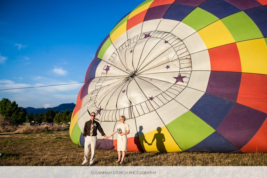a man and woman hold hands in front of colorful hot air balloon